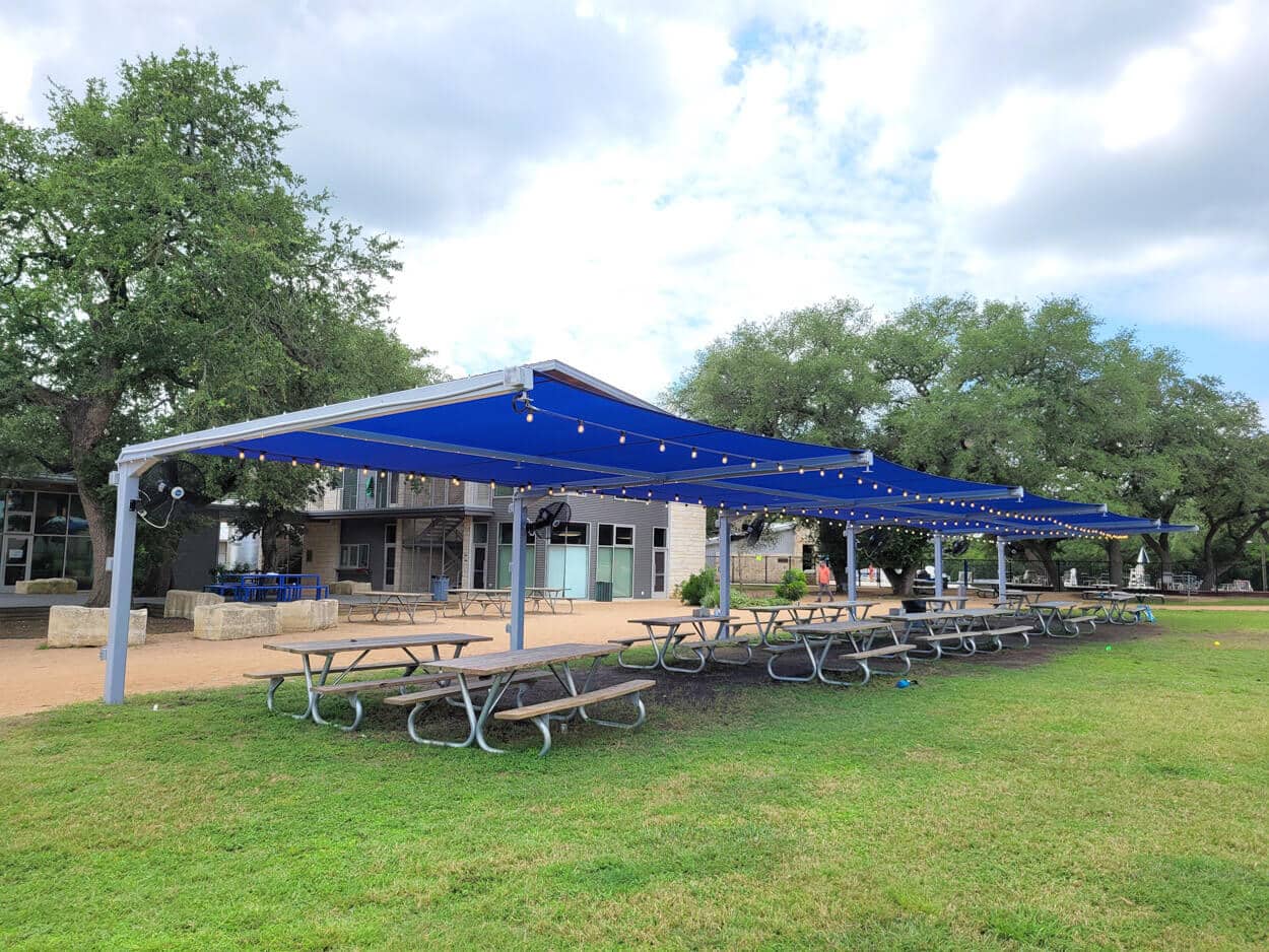 Commercial park benches installed under a cantilever shade at a playground in Cedar Park, Texas, offering comfortable seating and UV protection for visitors.